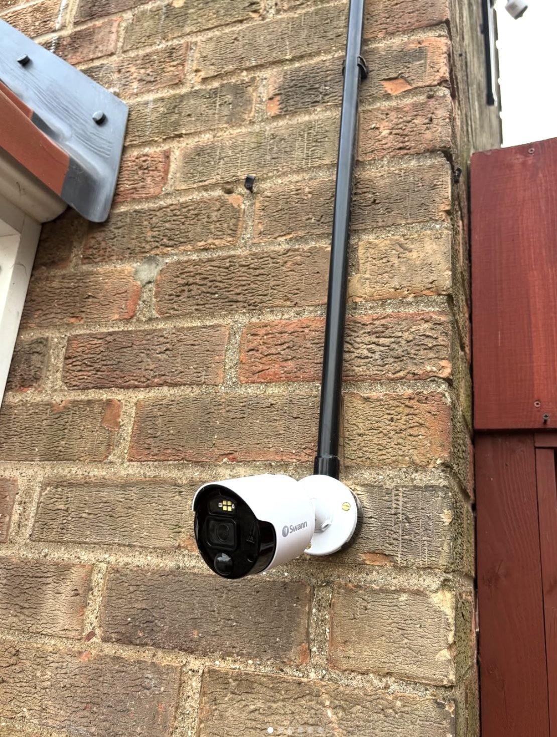 Swann CCTV camera installed on a brick wall beside a downpipe