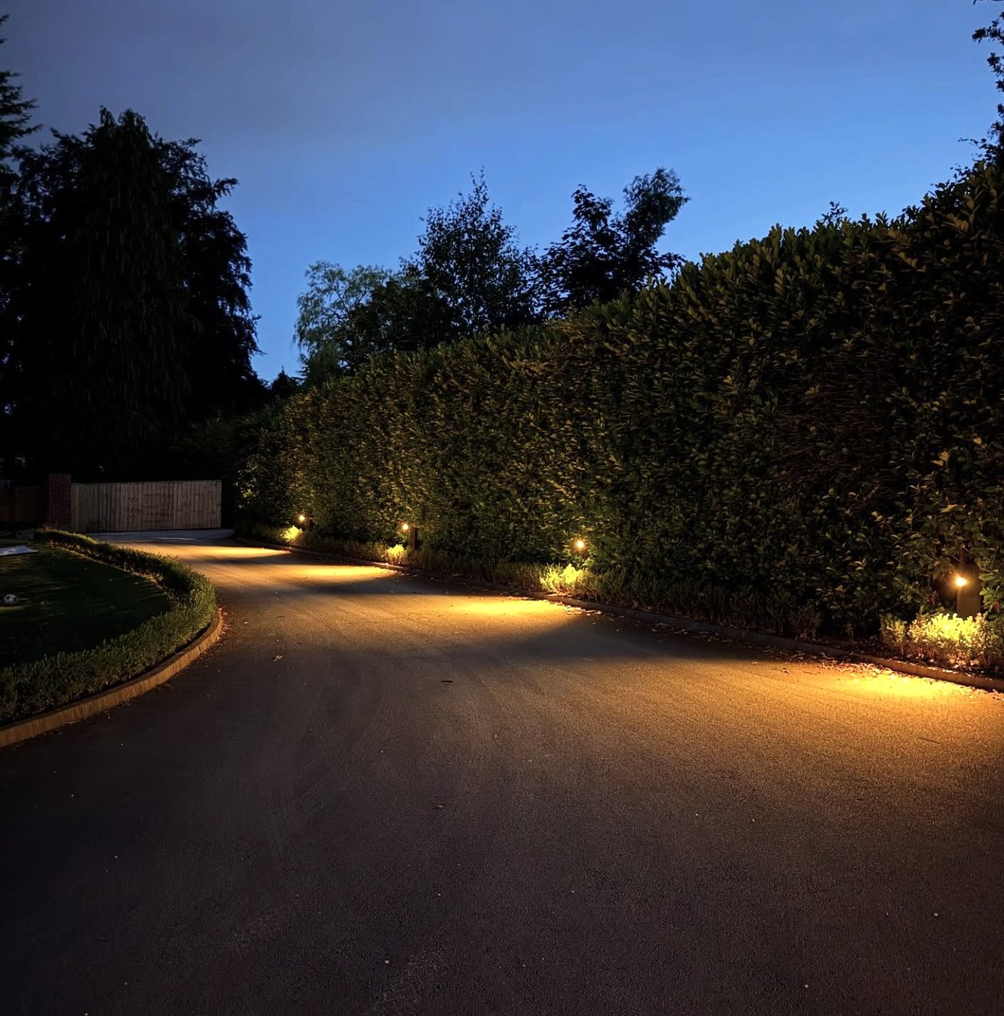 Driveway lit at dusk with bollard and border lighting along a hedge