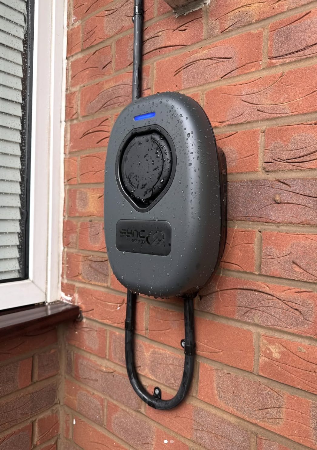 Sync Energy EV charger installed on a red brick wall in the rain